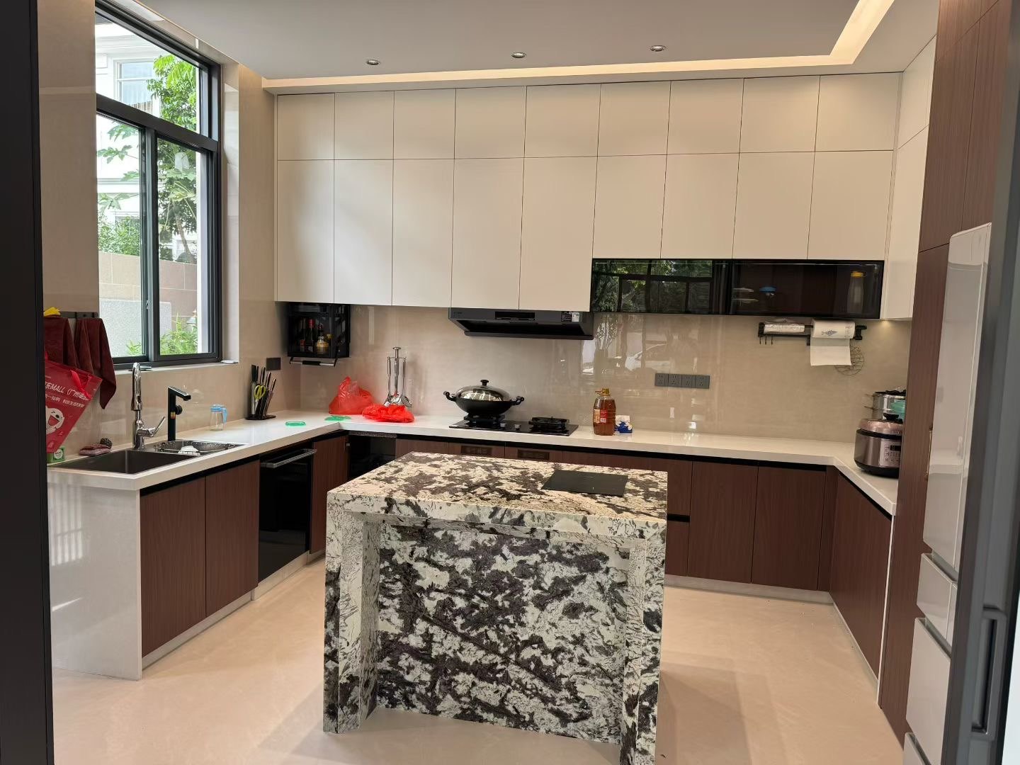 Kitchen with pale upper cabinetry, timber-tone lower cabinets and a patterned stone island